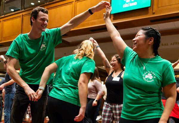 Two dancers wearing green shirts hold their arms up as another dancer ducks through.