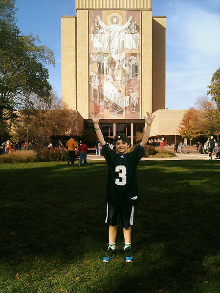 Small child poses outside of Hesburgh Library.