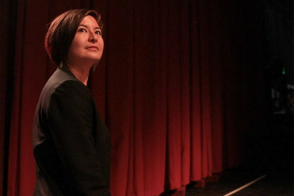 A woman with black hair wearing a black shirt looks out into a theatre.