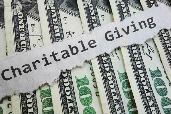 Graphic image of 100 dollar bills with a strip of paper running across it with the words "Charitable Giving" typed out on it.