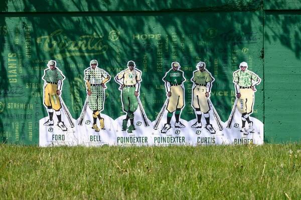 Paper cutouts of Black baseball players on a green outfield wall.