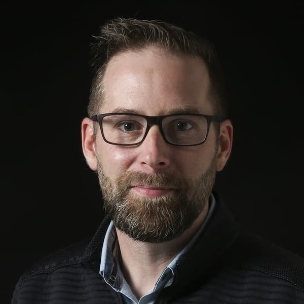 A man with glasses and a beard looks at the camera.