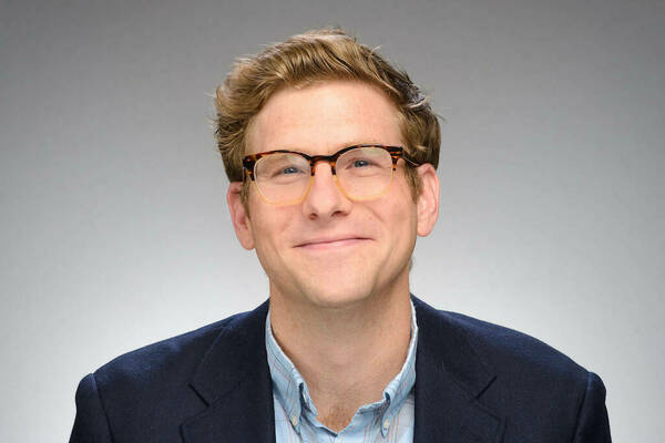 A man with brown hair and glasses, wearing a dark blue blazer.