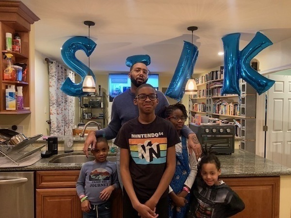 Joseph Earl Thomas, presenting as a black man, with his four children standing in a kitchen.