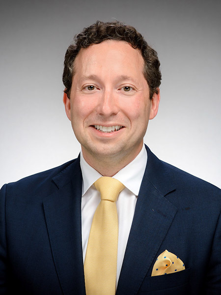 Kirk Doran, an associate professor of economics, presenting as a caucasian man with brown hair, wearing a blue suit and gold tie.