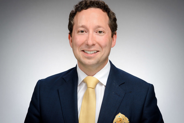 Kirk Doran, an associate professor of economics, presenting as a caucasian man with brown hair, wearing a blue suit and gold tie.