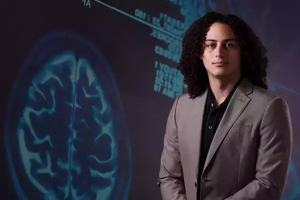 A photo of Austin Wyman in front of a background of a brain scan.