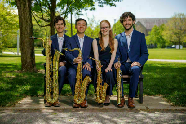 4 young people sitting on a bench with instruments.