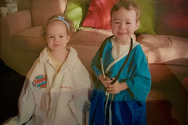 A young girl in an oversized white doctor's coat and a smiling boy in a blue robe holding a stethoscope.